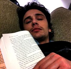 a man laying down reading a book with his eyes closed and one hand resting on an open book