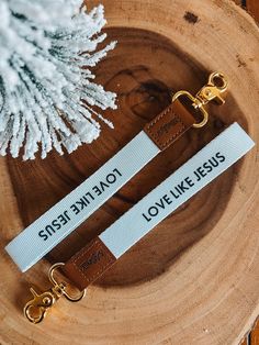 two leather key chains sitting on top of a wooden tree stump next to a white christmas tree