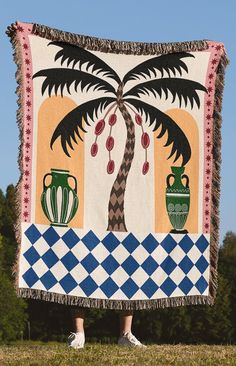 a person standing in front of a blanket with a palm tree and vases on it