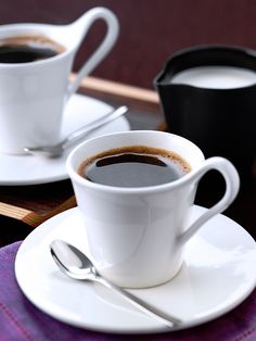 two cups of coffee sit on saucers next to each other