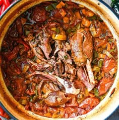 a pot filled with meat and vegetables sitting on top of a wooden table next to red peppers