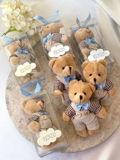 four teddy bears are in clear boxes with blue bows and tags on them, sitting next to a white flower