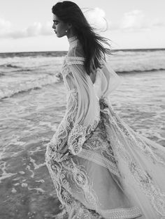 a woman standing on top of a beach next to the ocean wearing a long dress