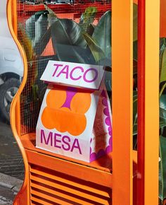 a taco stand with an orange carton and some plants in the back ground