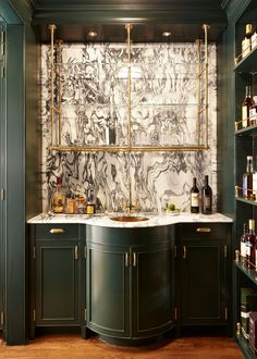 a kitchen with marble counter tops and green cabinets, along with wine bottles on shelves