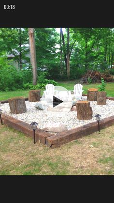 an outdoor fire pit made out of logs and gravel with chairs around it in the background