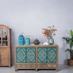 a wooden cabinet sitting next to a potted plant and vase on top of it