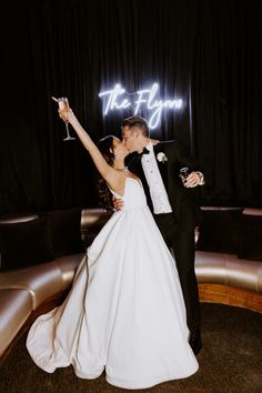 a bride and groom pose for a photo in front of the neon sign at their wedding reception