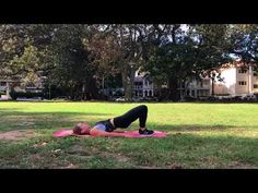 a woman laying on top of a pink yoga mat in a park next to trees