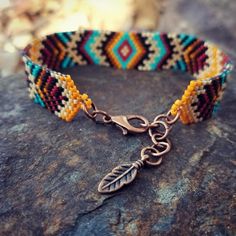 a bracelet with a leaf charm on it sitting on top of a rock next to rocks