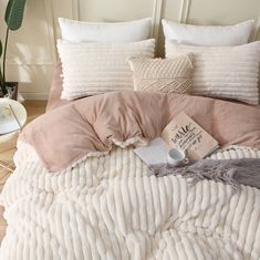 a bed covered in blankets and pillows with a book on the pillow case next to it