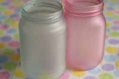 two jars sitting on top of a table covered in polka dot fabric, one pink and the other white