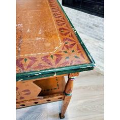 an old table has been painted with colorful designs on it and sits in front of a brick fireplace