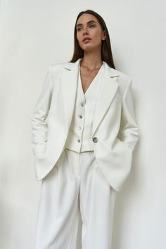 a woman standing in front of a white wall wearing a white suit and matching heels