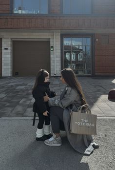 two women sitting on a bench in front of a brick building talking to each other