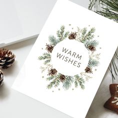 a christmas card with the words warm wishes surrounded by pine cones and fir branches on a white background