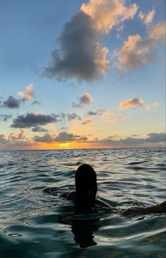 a woman swimming in the ocean at sunset with clouds and blue sky above her head