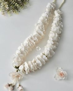 white flowers and pearls are arranged on a table next to a necklace, earring and ring