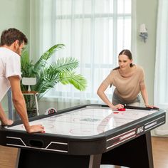 a man and woman playing a game of air hockey in the living room at home