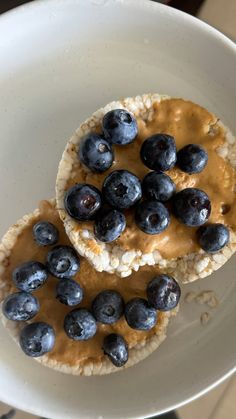 two desserts with blueberries and peanut butter on top in a white bowl, ready to be eaten