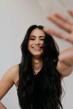 a woman with long black hair smiling and holding her hands up in the air,