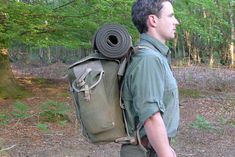 a man in the woods with a roll up backpack on his back, looking at something