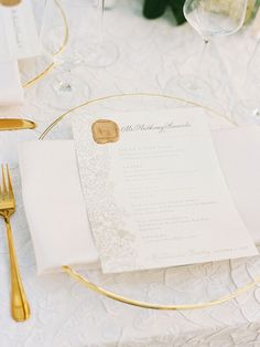 the table is set with white linens and gold place settings, along with silverware