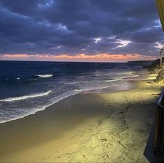 a beach with waves coming in to the shore and dark clouds over the water at sunset