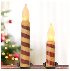 two lit candles sitting next to each other in front of a christmas tree