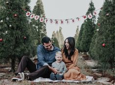 a family sitting on a blanket in front of christmas trees with the words merry christmas