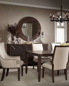 a dining room table with chairs and a round mirror on the wall above it in front of a window