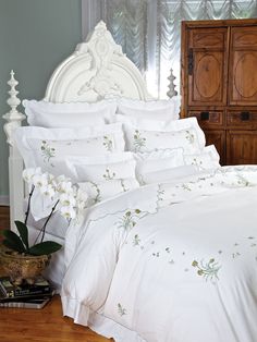 a bed with white comforters and flowers on it in a room next to a dresser