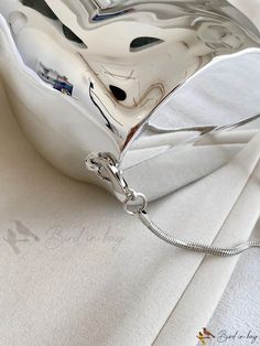 a shiny silver purse sitting on top of a white cloth covered tablecloth with a chain hanging from it's side