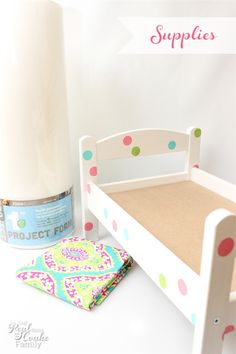 a white doll bed next to a roll of toilet paper on a table with a pink and green polka dot pillow