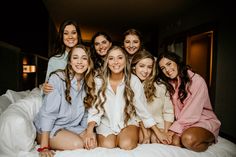 a group of young women sitting next to each other on top of a white bed