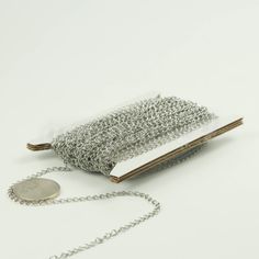 a roll of silver chain sitting next to a purse on a white surface with a coin in it