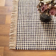 a vase filled with flowers sitting on top of a wooden floor next to a rug