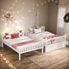 two white beds in a bedroom with string lights on the wall and wooden flooring