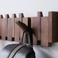 a wall mounted coat rack with two coats hanging on it's sides and a leather bag in the foreground