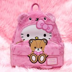 a pink hello kitty backpack with a teddy bear on the front and back pocket, sitting on a fluffy pink surface