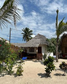 a white house with a thatched roof and palm trees in the foreground on a sandy beach