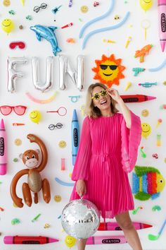 a woman in a pink dress standing next to a wall covered with toys and letters