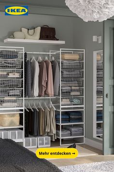 an open closet with clothes hanging on shelves and baskets in front of it, next to a bed