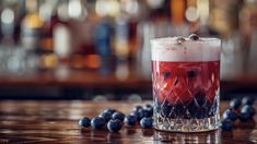 a glass filled with liquid and blueberries on top of a wooden table next to a bar