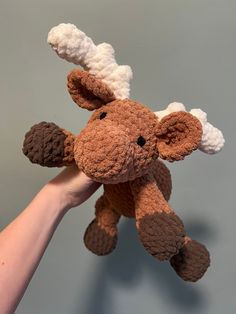 a hand holding a brown and white stuffed animal with antlers on it's head