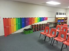 an empty classroom with rows of red chairs and rainbow colored wall behind the desks