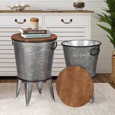 two metal buckets sitting on top of a rug next to a white dresser and potted plant