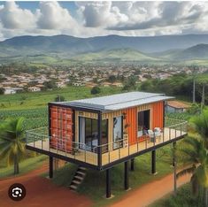 a house made out of shipping containers on top of a dirt road with palm trees and mountains in the background