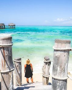 a woman standing on the beach looking out at the ocean and pier in the distance