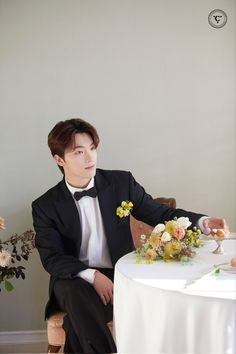 a young man in a tuxedo sitting at a table with flowers on it